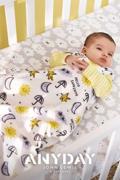 a baby laying on top of a bed next to a yellow and white crib