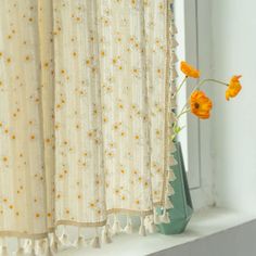 an orange flower sitting on top of a window sill in front of a curtain