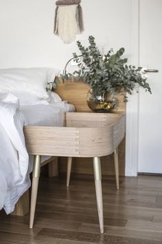 a bed with white sheets and pillows in a bedroom next to a plant on a wooden table