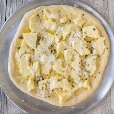 an uncooked pizza sitting on top of a metal pan covered in cheese and herbs