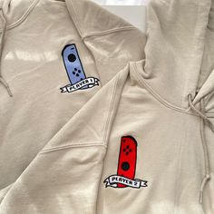 Displayed are two beige hoodies from the petimint collection, part of the Pack 2 Hoodie Player 1 & 2 Gamer Apparel set. Each hoodie features an embroidered design of a game controller on the chest—one in blue labeled Player 1 and the other in red labeled Player 2. Perfect for any gamer, this gaming apparel showcases controllers with similar shapes and button layouts. Gaming Gifts For Him, Couple Hoodies Relationships, Couples Tshirt Ideas Matching, Couples Hoodies Ideas, Cute Matching Hoodies, Couple Hoodies Ideas Design, Matching Sweatshirts For Couples, Matching Couples Hoodies, Friend Sweatshirts