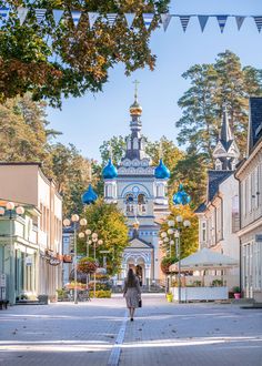 a woman is walking down the street in front of an old church with blue domes