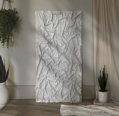 a large white piece of paper sitting on top of a wooden floor next to a potted plant