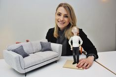 a woman sitting at a table with a doll next to her and a couch in the background