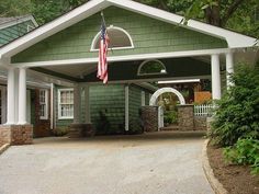 a green house with an american flag hanging from it's front door and porch