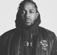 a man with dreadlocks standing in front of a white wall wearing a black jacket