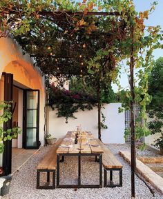 an outdoor dining area with wooden benches and table set up for dinner under the pergolated trellis