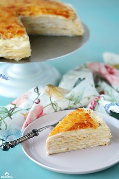 a piece of cheesecake on a plate with a fork next to it and a cake in the background