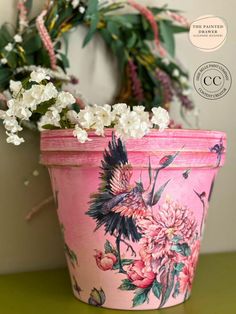 a pink flower pot sitting on top of a green table next to a white wreath