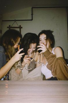 three girls are drinking wine and laughing together at a party with their hands in the air