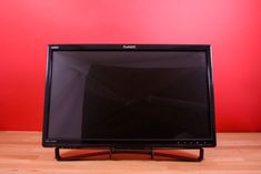 a flat screen tv sitting on top of a wooden table next to a red wall