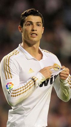 a man holding a soccer ball in his right hand and wearing a white shirt with gold stripes