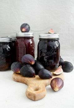 figurines and plums sit on a cutting board next to jars with jam in them