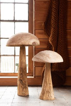 two wooden mushrooms sitting on top of a white tile floor next to a large window