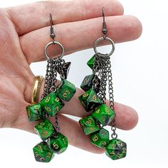 a pair of green and black dice earrings with numbers on them, being held by a person's hand