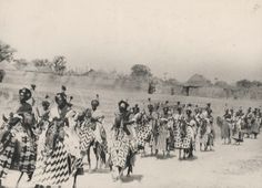 an old black and white photo of people dressed in native clothing walking down a dirt road