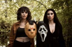 two women standing in the woods with masks on their faces and one wearing a mask