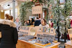 two women are looking at an assortment of jewelry on display in a store with people standing around