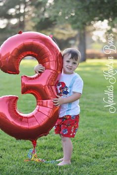 a young boy holding a large red balloon in the shape of the number 3,