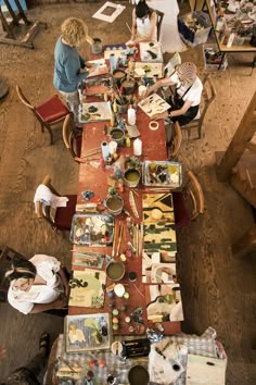 an overhead view of people sitting at a long table covered in art supplies and papers