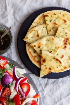 some pita bread on a black plate next to a bowl of salad and a glass of ketchup