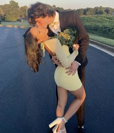 a man kissing a woman on the cheek while standing next to an asphalt road with trees in the background