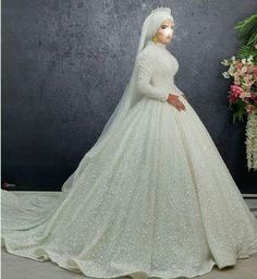 a woman in a white wedding gown with a veil on her head and flowers behind her