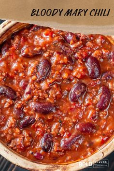 a bowl filled with chili and beans on top of a wooden table next to a paper bag