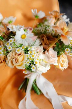 a bridal bouquet with white and peach flowers on an orange cloth draped over it