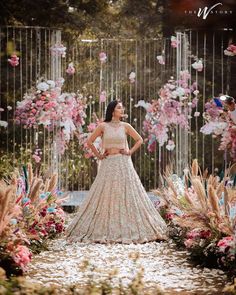 a woman standing in front of flowers wearing a long skirt and crop top, with her hands on her hips