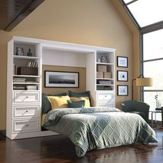 a white bed sitting under a window next to a wooden floor