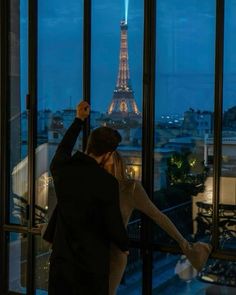 a man and woman standing in front of a window looking out at the eiffel tower