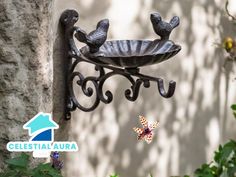 a metal bird feeder hanging from the side of a building with butterflies flying around it