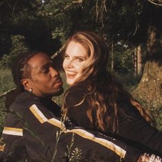 a man sitting next to a woman on top of a lush green forest filled with trees