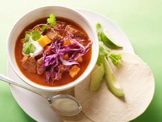 a white bowl filled with soup next to a tortilla on a green table