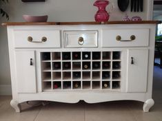 a white cabinet with wine bottles in it on top of a tile floor next to a wall