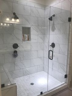 a walk in shower sitting next to a white tiled wall and floor with black handles