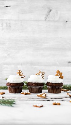 three cupcakes with white frosting and gold decorations on them sitting on a table