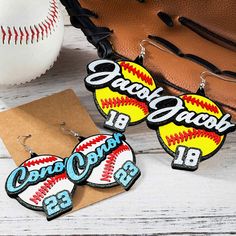 three baseball themed earrings sitting on top of a wooden table next to a catchers mitt