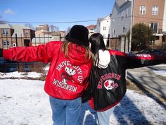 two people standing in the snow with their arms spread out and one person wearing a red jacket