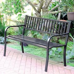 a metal bench sitting on top of a brick walkway next to a potted plant