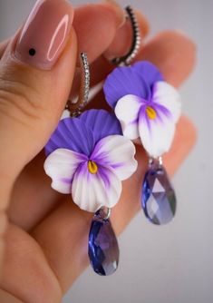 a woman's hand holding three purple and white flowers with crystal tears on them