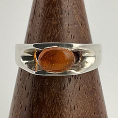 a silver ring with an orange stone on it sitting on top of a wooden stand