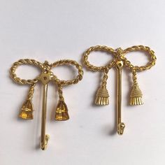 two gold toned metal items with bells and tassels attached to them on a white surface