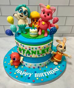 a birthday cake with cartoon characters on top and balloons in the shape of animals sitting around it