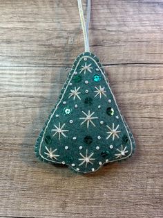 a green christmas tree ornament hanging from a string on a wooden table with snowflakes