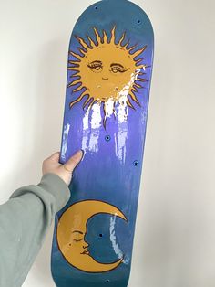 a person holding up a skateboard with the sun and moon painted on it's side