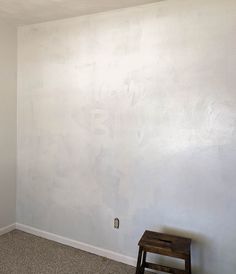 an empty room with white walls and a small wooden stool in the corner next to it