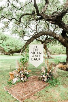 a sign that says to the moon and back under a tree with flowers on it