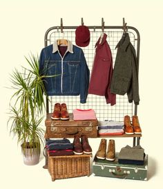 clothes and shoes are hanging on a rack next to a potted plant in front of an old suitcase